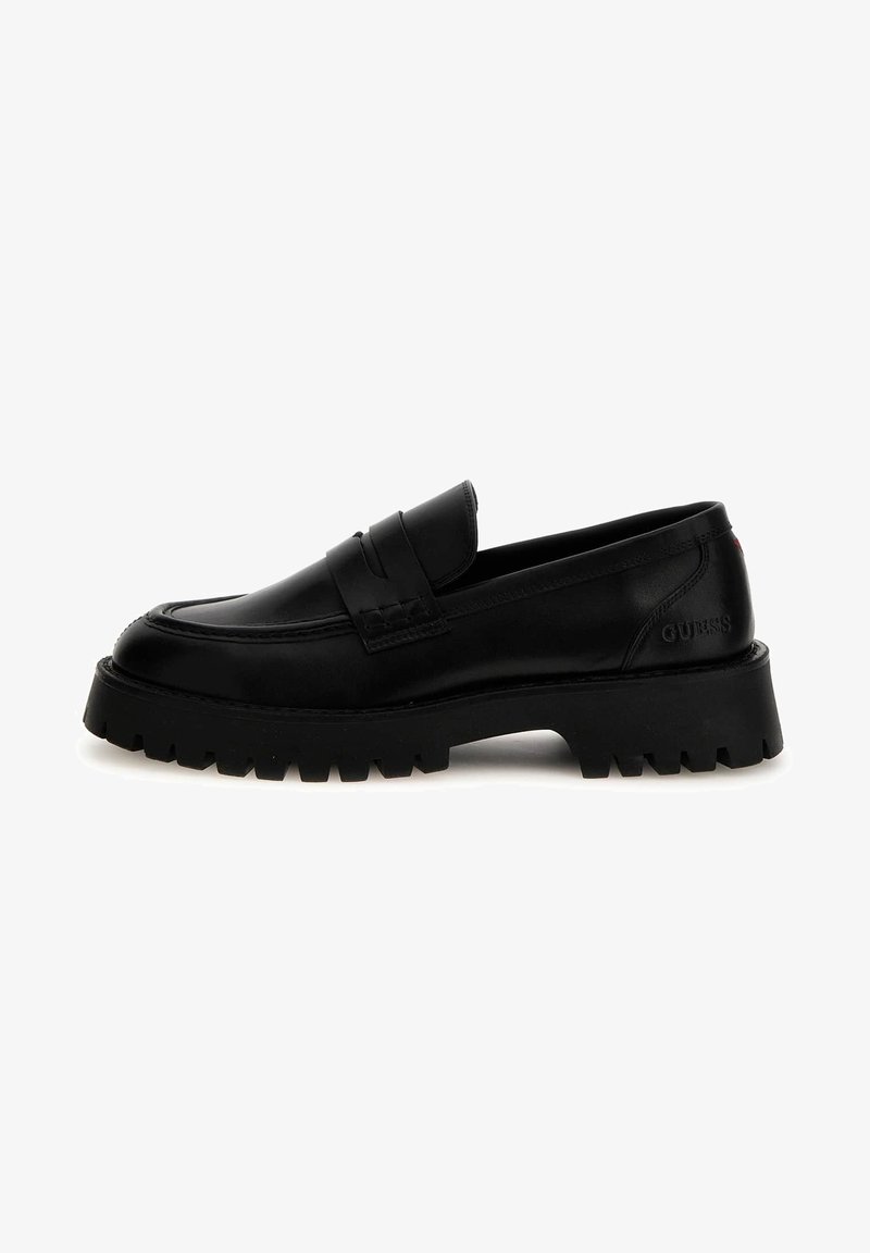 Mocassins de couro preto com uma sola grossa e canelada. Apresenta um bico de mocassim cosido e uma tira frontal. A marca é visível no calcanhar.