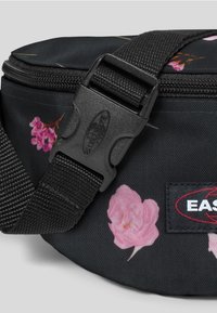 Černá látková ledvinka s nastavitelným popruhem, plastovou sponou, zipem, růžovým květinovým potiskem a obdélníkovou nášivkou s logem na přední straně.