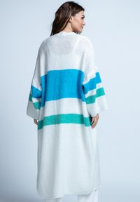 Długi, oversize kardigan w białym splocie z szerokimi poziomymi paskami w kolorach turkusowym, niebieskim i zielonym. Posiada rękawy o długości 3/4 oraz luźny krój.