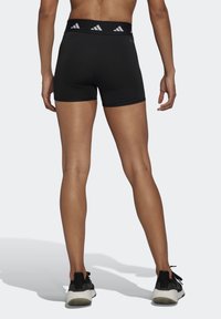 Mustat urheilushortsit, joissa on leveä joustava vyötärö, jossa on valkoiset kolmi-palkki-bränditykset. Valmistettu joustavasta ja sileästä materiaalista, muotoilu istuu hyvin.