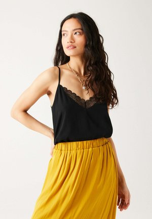Camisole noire avec des détails en dentelle, associée à une jupe maxi plissée jaune. Le haut présente des bretelles fines et une coupe décontractée.