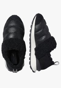 Scarpe slip-on nere con tomaia in pelle texturizzata, colletto in peluche, suola bianca e suola in gomma con battistrada per una migliore aderenza.