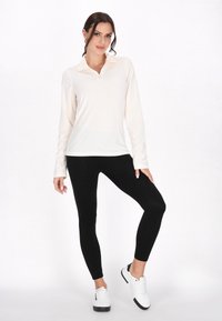 Lys beige zip-up langærmet toppar med sorte leggings og hvide sneakers. Toppen har en blød tekstur og en tætsiddende silhuet.