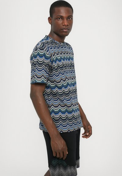 Chemise à manches courtes avec un motif en zigzag bleu, vert et gris. Fabriquée en tissu léger, avec un col rond et une coupe décontractée.