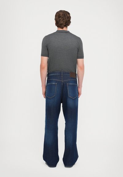 Jean en denim avec une silhouette évasée, couleur bleu foncé et coutures contrastées. Comprend deux poches arrière et une étiquette en cuir marron au niveau de la taille.