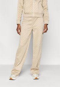 Μπεζ φόρμα με επαναλαμβανόμενο μοτίβο λογοτύπου, που περιλαμβάνει ζακέτα με φερμουάρ και παντελόνι που ταιριάζει. Λείο υλικό με ριμπ μανσέτες και πλαϊνές λεπτομέρειες.