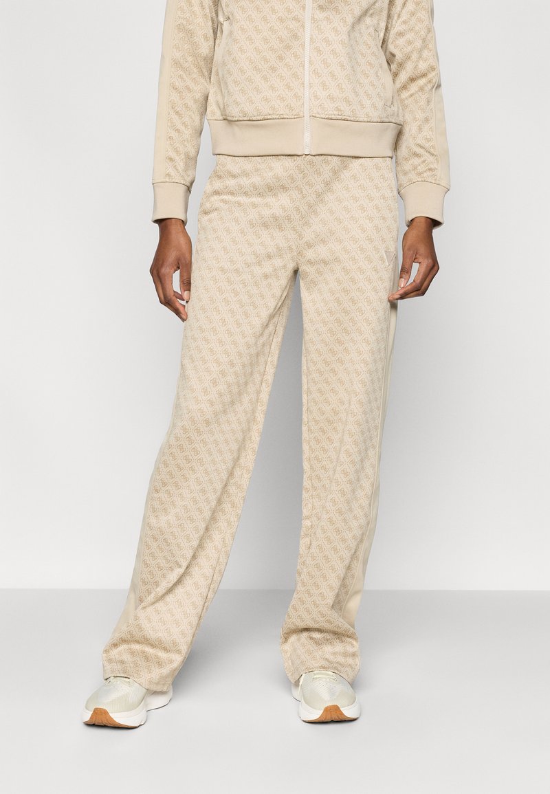 Μπεζ φόρμα με επαναλαμβανόμενο μοτίβο λογοτύπου, που περιλαμβάνει ζακέτα με φερμουάρ και παντελόνι που ταιριάζει. Λείο υλικό με ριμπ μανσέτες και πλαϊνές λεπτομέρειες.