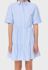 Abito camicia azzurro chiaro a maniche corte con bottoni sul davanti, colletto rotondo, vita elastica e gonna a strati arricciata. Tessuto liscio.