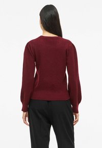 Bordowy sweter z dzianiny z fakturowanym wzorem, długimi bufkami oraz ściągaczem u dołu. Tył zaprojektowany tak, aby podkreślał dopasowaną sylwetkę.