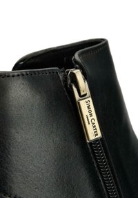 Black leather ankle boot featuring a side zip closure with a gold-tone metal pull tab. Slightly textured upper, minimalist design.