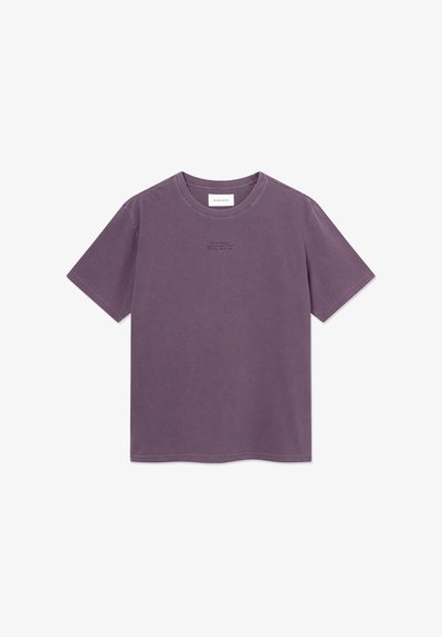 Lilla bomulls t-skjorte med korte ermer, rund hals og liten tekstlogo i en mørkere nyanse på brystet. Minimalistisk design.