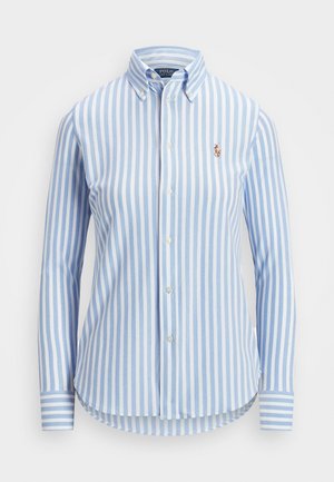 Chemise à manches longues avec boutons, rayures verticales bleues et blanches, et petit logo brodé sur la poitrine gauche.