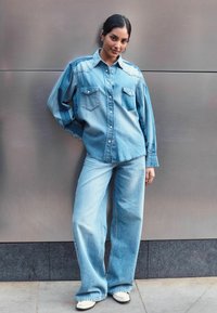 Hele sinine denimsärk kahe rinnataskuga, millele on paari pandud laiad helesinised teksad. Mõlemal rõivakul on lõdva lõike ja klassikaline õmblus.