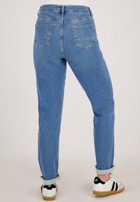 Lichtblauwe denim jeans met opgerolde pijpen, achterzakken en een slim fit. Gecombineerd met witte sneakers met zwarte accenten.