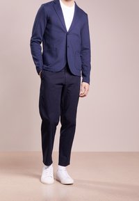 Námořnická blazerka se dvěma předními kapsami, kombinovaná s tmavými kalhotami a bílými teniskami. Blazerka má hladkou texturu a moderní střih.