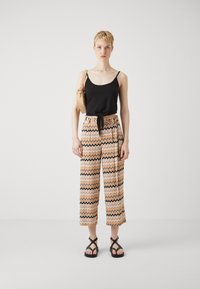 Svart ermeløs topp med knytefront, mønstrede vide bukser i oransje, krem og marineblå sikk-sakk design, kombinert med svarte sandaler med stropper.