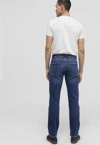Jeans de denim azul oscuro con corte recto, que presentan dos bolsillos traseros y costuras en contraste. Combinando con una camiseta blanca sencilla.