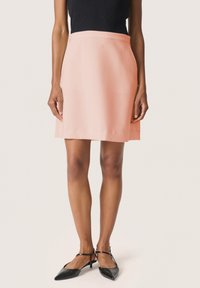 Rausvai A forma sijonas, pagamintas iš lengvos medžiagos, pasižymi lygiu paviršiumi ir vidutinio ilgio dizainu. Suderintas su juodais smailiais bateliais.