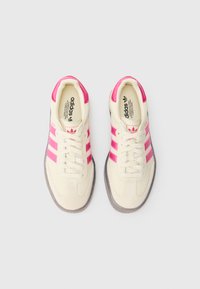 Krēmkrāsas sporta apavi ar rozā akcentiem un trim svītrām, ar fakturētu zamša apdari un gumijas zolēm.