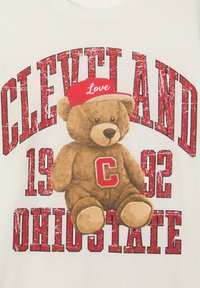 Biała koszulka z grafiką brązowego pluszowego misia w czerwonej czapce z napisem "Miłość", z napisem "CLEVELAND 1992 OHIO STATE" w pogrubionej czerwonej czcionce.