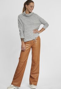 Maglione grigio a maniche lunghe con collo a cowl in tessuto testurizzato; abbinato a pantaloni in ecopelle marroni a vita alta e gamba larga e sneakers bianche.