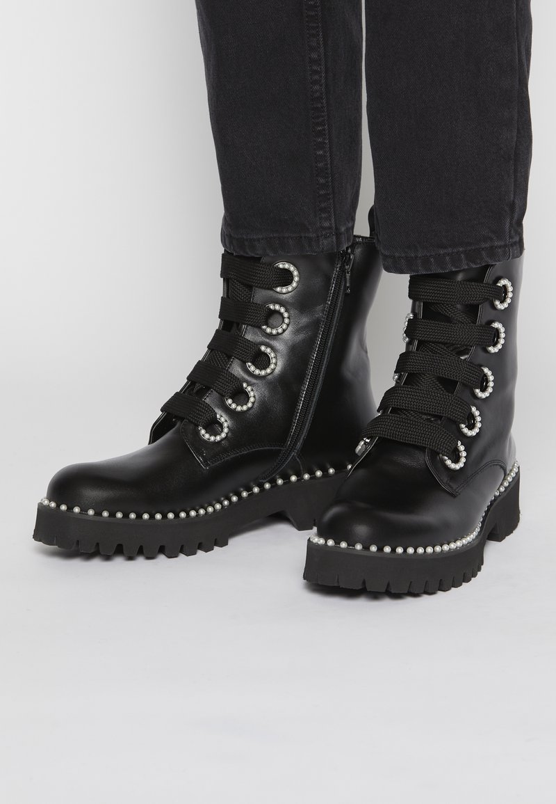 Bottes noires en cuir, à la cheville, avec des semelles épaisses, des œillets sertis de perles et des garnitures, portées avec un jean noir.