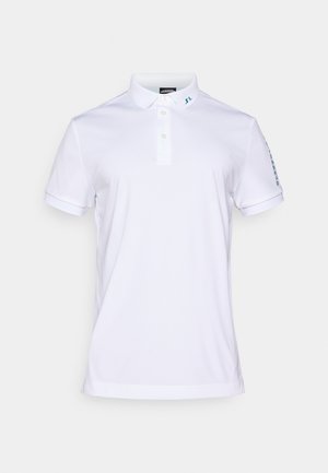 Bela polo majica iz teksturiranega materiala, ki ima ovratnik, tri gumbe in subtilno modro blagovno znamko na ovratniku in rokavu.
