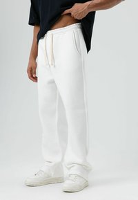 Witte katoenen joggingbroek met elastische tailleband en trekkoorden, voorzien van zijzakken en een comfortabele pasvorm, gecombineerd met witte sneakers.