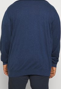 Pletený svetr v tmavě modré barvě, s volným střihem, dlouhými rukávy a žebrovaným lemem. Texturovaná látka s hladkým povrchem.