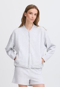 Sweatshirt zippé gris clair avec une coupe décontractée, col côtelé, épaules tombantes et poches latérales, associé à un short assorti.