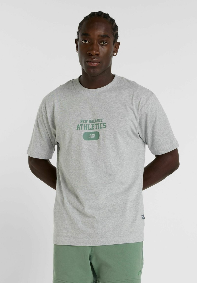 Grå kortærmet t-shirt med "NEW BALANCE ATHLETICS" trykt i grønt. Fremstillet af blødt stof, med rund hals og afslappet pasform.