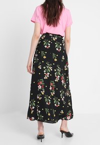 Černá květinová sukně s barevnými květinovými vzory, nošená s růžovým topem. Sukně je po kotníky s volným střihem a jemnými puntíky.