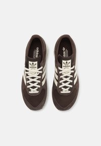 Brown suede and mesh sneakers with white laces and three white stripes. Features a padded collar and logo tag on the tongue.