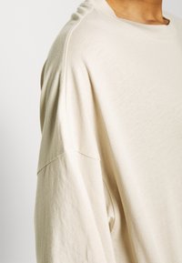 Beige oversized sweatshirt gemaakt van zacht materiaal met een ontspannen pasvorm, voorzien van een ronde halslijn en verlaagde schoudernaad voor comfort.