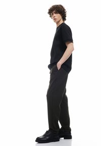 Sort kortærmet T-shirt parret med mørkebrune bukser og sorte sko. Outfittet har en afslappet pasform og minimalistisk design.