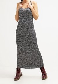 Šedý melírovaný maxi šaty s přiléhavým korzetem, tenkými ramínky a bočními rozparky, doplněné burgundskými šněrovacími botami. Měkká, texturovaná tkanina.