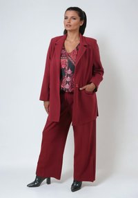 Burgundy suit with a structured blazer and wide-leg pants. Underneath, a patterned top in black and pink. Finished with black heeled boots.