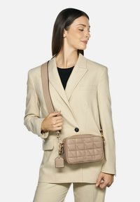 Borsa a tracolla beige realizzata in pelle trapuntata con forma rettangolare, caratterizzata da un accento in metallo dorato e un'etichetta removibile.