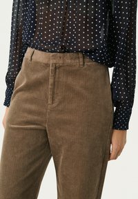 Marineblauwe doorschijnende blouse met witte stippen en bruine corduroy broek met verticale strepen. Blouse heeft lange mouwen en een ontspannen pasvorm.