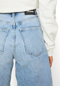 Vaqueros de mezclilla azul claro con un ajuste relajado. Cuenta con dos bolsillos traseros y una etiqueta negra con "DR.DENIM" en la cinturilla.