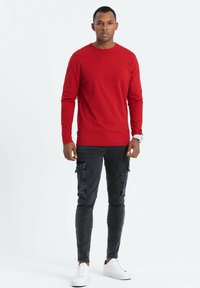 Rode langetermijnshirt met een aansluitend ontwerp, gecombineerd met zwarte cargobroeken met meerdere zakken en witte sneakers. Eenvoudige stijl en effen kleuren.