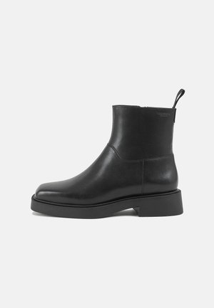 Schwarzer Lederankle Boot mit abgerundetem Zeh, Zuglasche hinten und niedrigem Absatz auf schlichtem hellem Hintergrund.