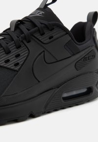 La sneaker Nike Air Max noire présente une tige texturée, un branding prominent, un système de laçage et un amorti à air visible dans la semelle.