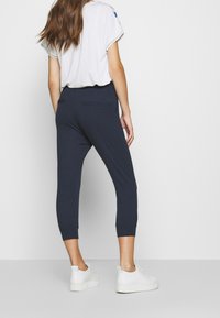 Marinblå korta joggers med mjuk textur, elastiskt midjeband och två bakfickor. Matchas med en vit topp med korta ärmar och vita sneakers.