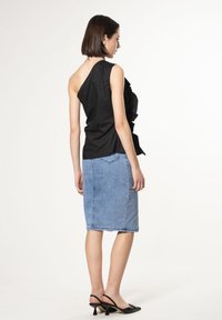 Zwarte asymmetrische top met ruffle-detail, gecombineerd met een lichtblauwe denim pencil skirt. Zwarte hakken maken de outfit compleet.