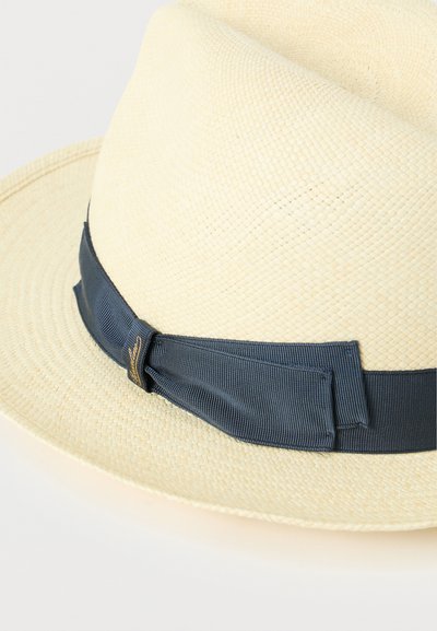 Καπέλο φεράδορ από ψάθα σε φυσικό χρώμα με φαρδιά ζώνη από σκούρο μπλε ύφασμα, με υφασμένη υφή και κλασικό σχήμα. Λεπτομέρειες με χρυσή απόχρωση.