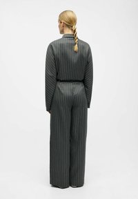 Salopette à jambes larges en gris foncé avec des rayures verticales, dotée d'un col, de manches longues et d'une taille ceinturée pour un ajustement structuré.