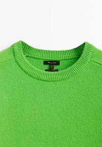 Pull en cachemire vert, col rond, col et poignets côtelés, texture douce, étiquette de marque minimaliste située à l'intérieur du col.