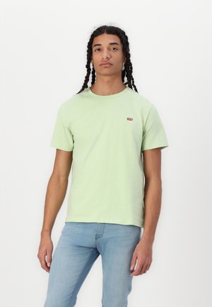 Lys grøn t-skjorte i bomull med korte ermer og rund hals, med en liten rød Levi's-logo på venstre bryst. Brukt sammen med blå jeans.