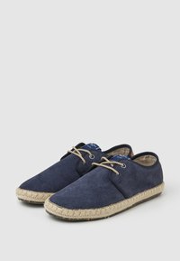 Zapatos de ante azul marino con punta redondeada, suela de yute y cordones beige. Presentan una textura suave y una etiqueta de marca en la lengüeta.